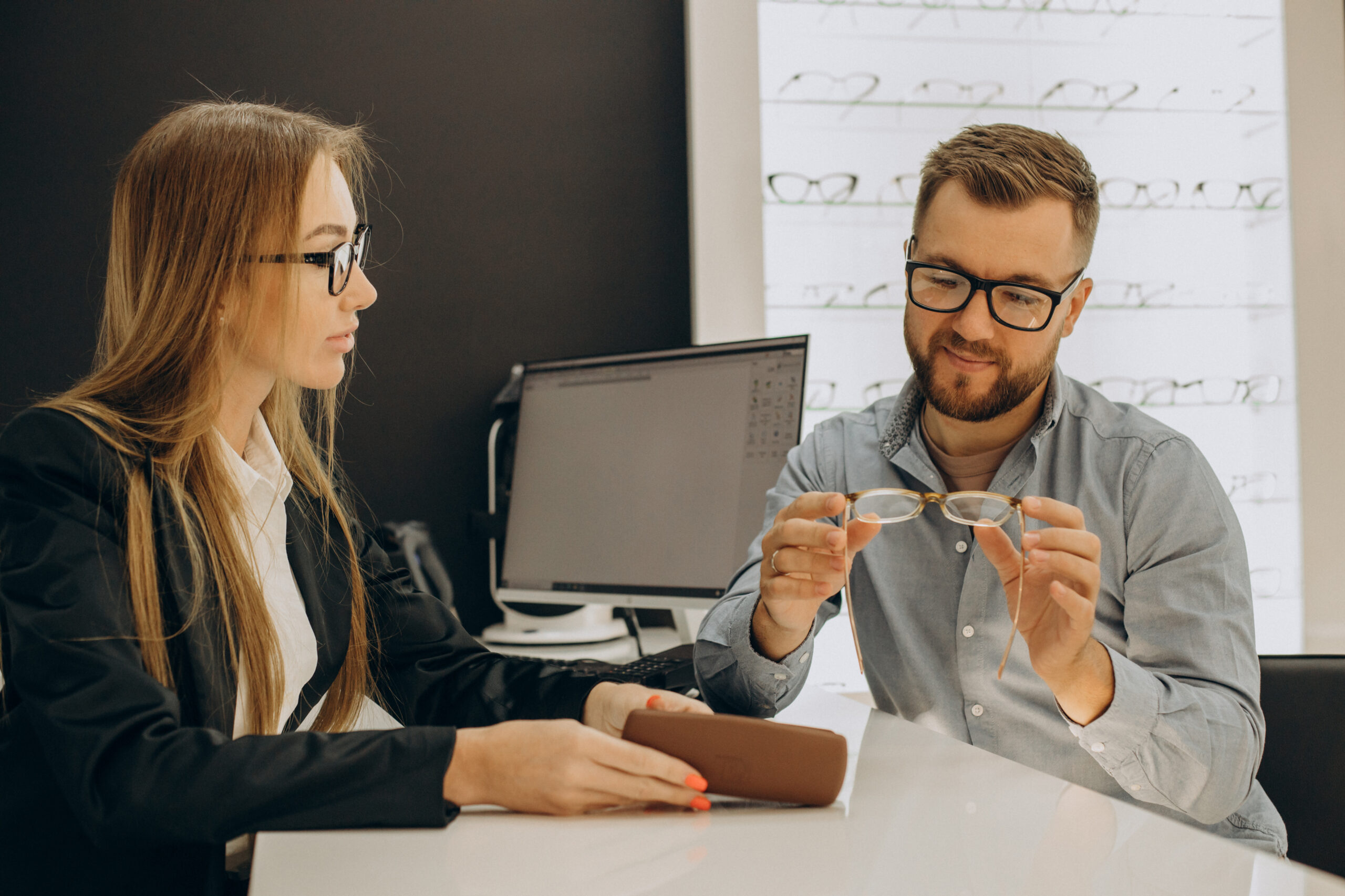 Customer shoosing spectacles at optic store with the lelp of sales person
