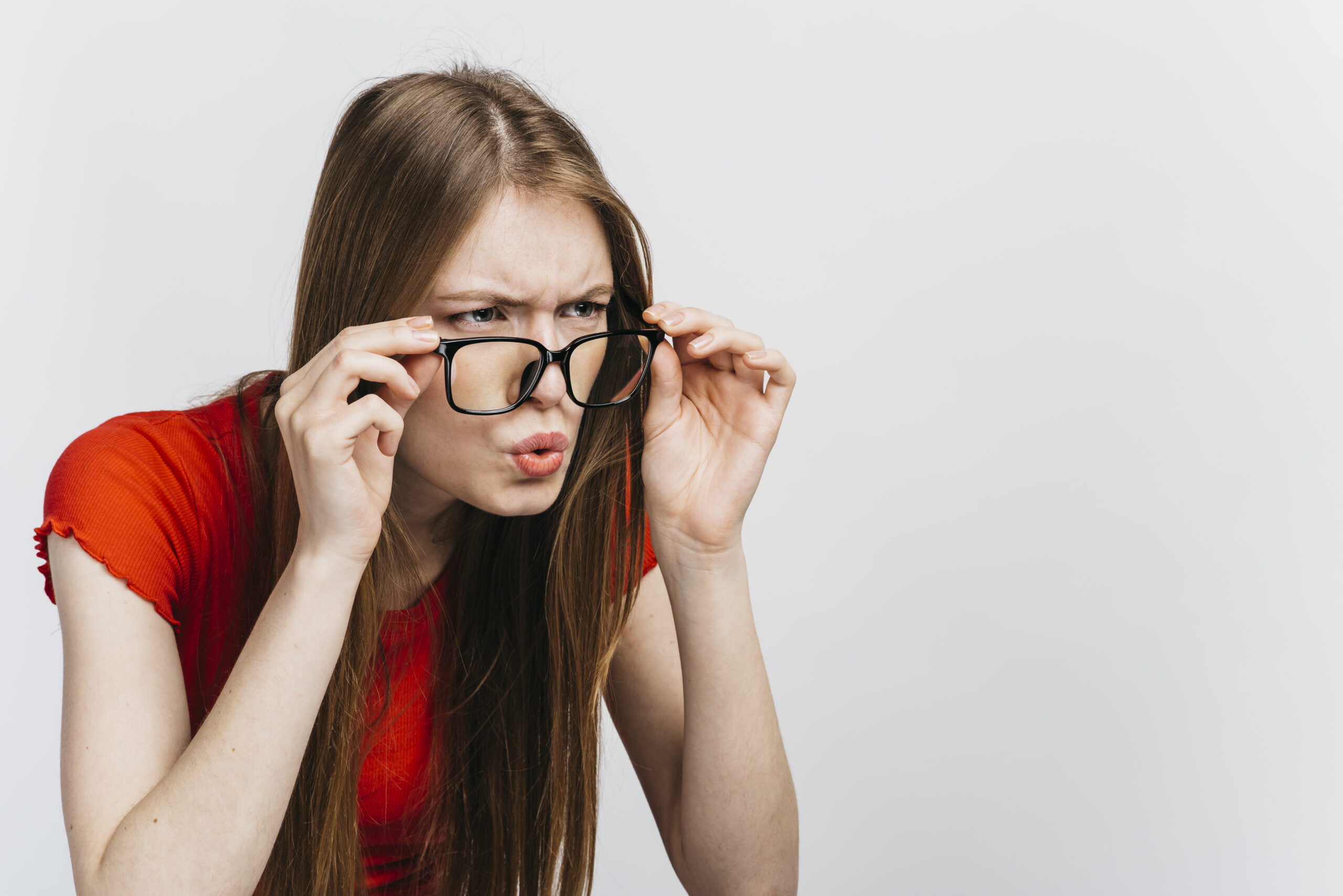 A young woman squints through her glasses with curiosity, trying to see something clearly.